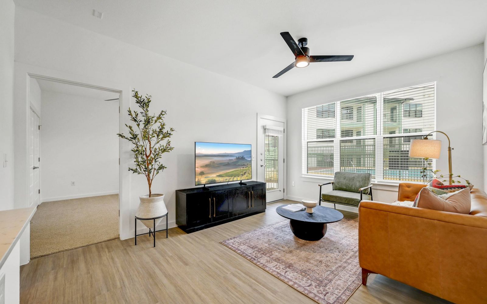 Bright living room with a brown sofa, TV, plant, coffee table, rug, and large windows. at Bluff View at Frederick Creek.