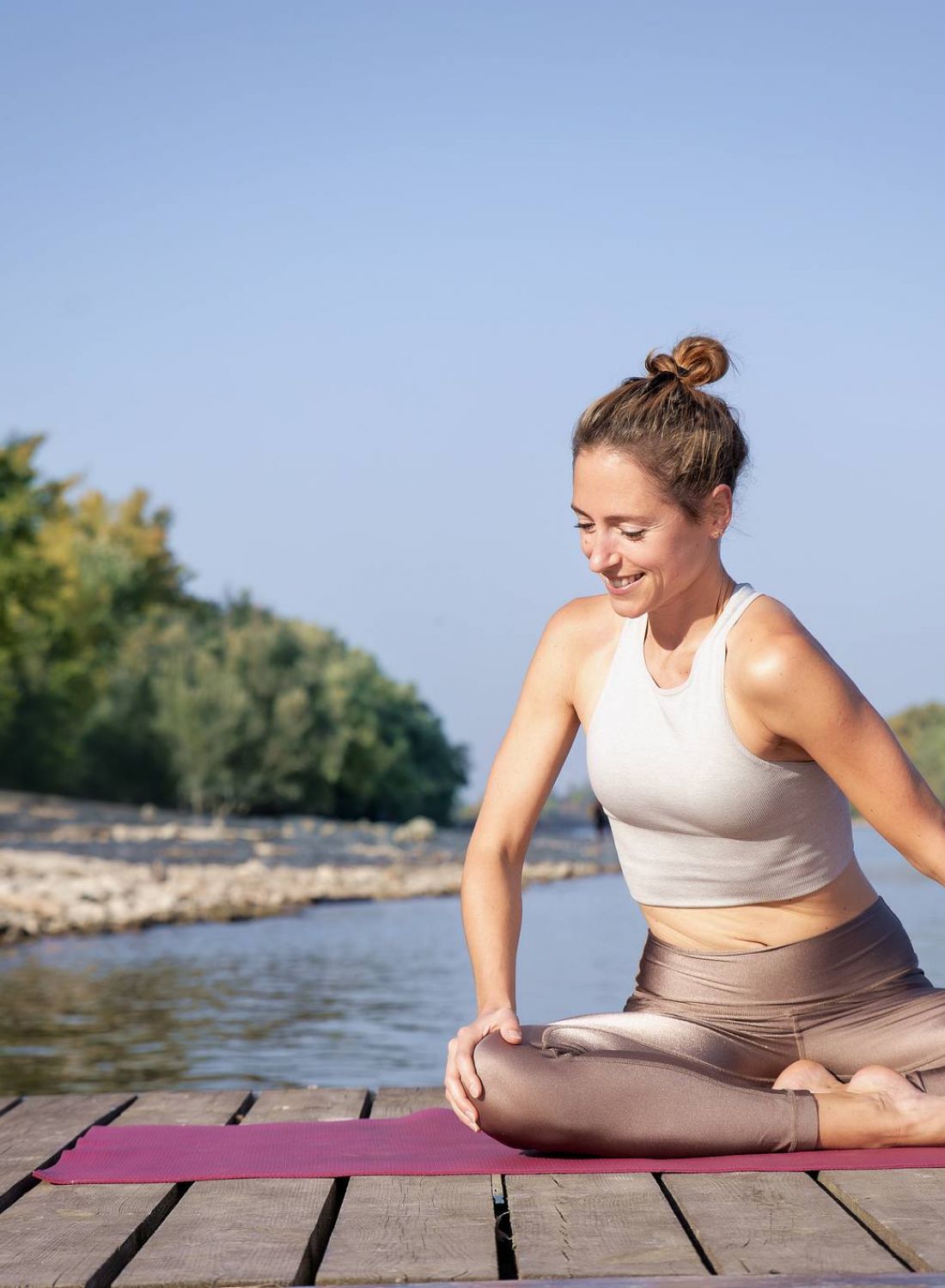 Woman doing yoga in a seated pose on a dock by the water, surrounded by trees, on a sunny day. at Bluff View at Frederick Creek.