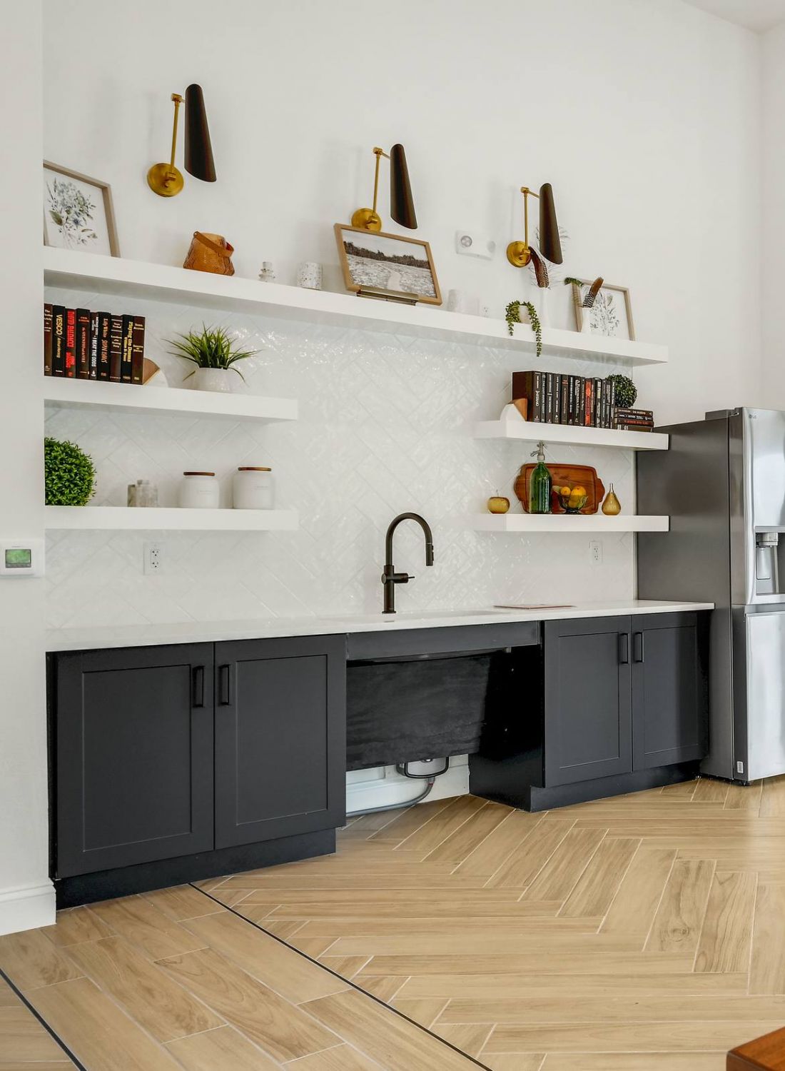Modern kitchen area with black cabinets, open shelves, a fridge, bar stools, and wood-look flooring at Bluff View at Frederick Creek.