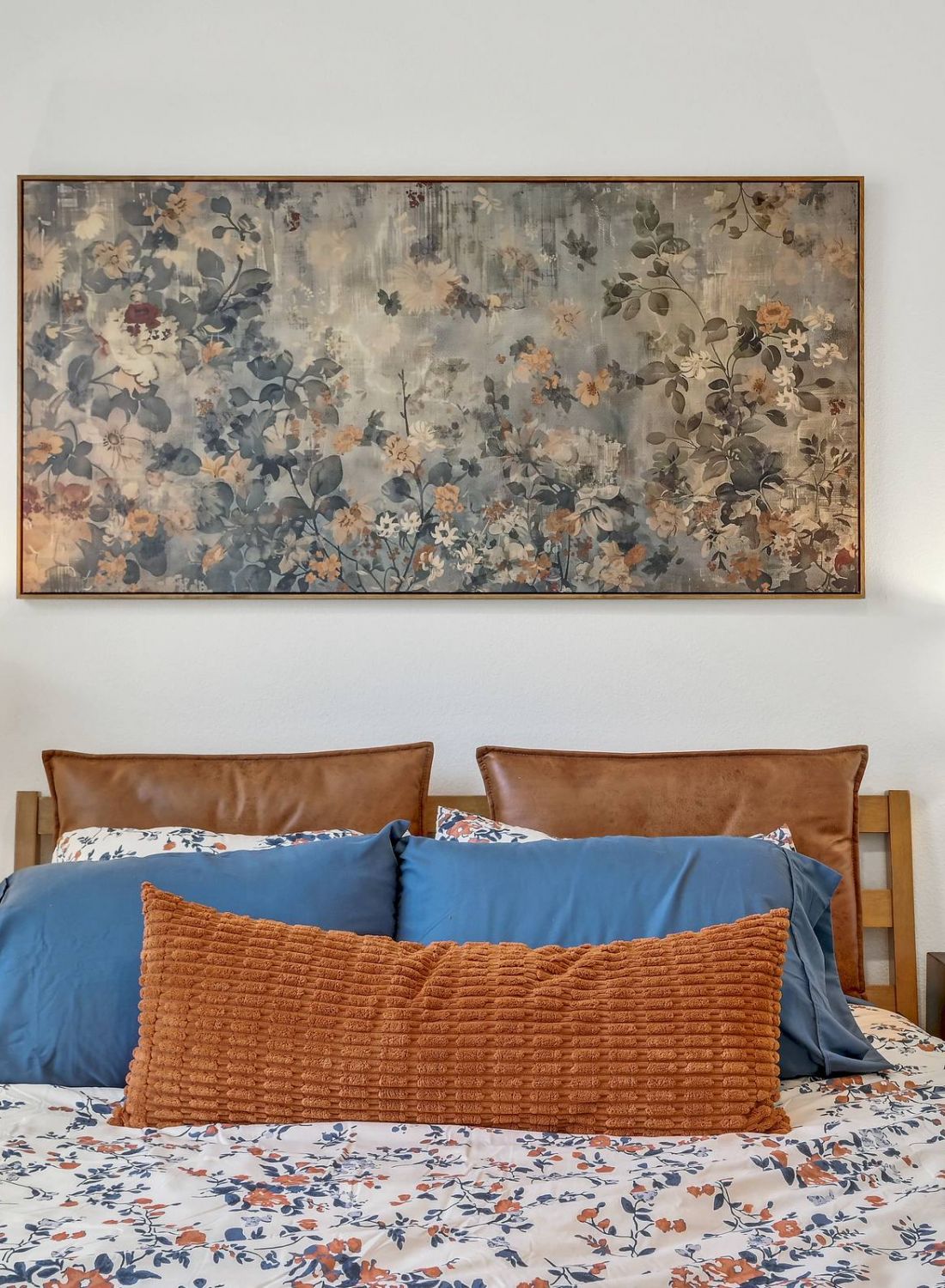 Cozy bed with blue and orange pillows, floral bedding, two lamps, and floral artwork above the headboard. at Bluff View at Frederick Creek.