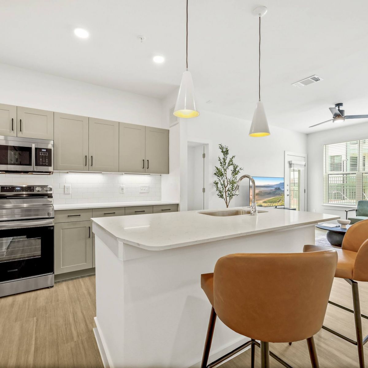 Modern kitchen with island, barstools, stainless steel appliances, and open living area with large windows at Bluff View at Frederick Creek.