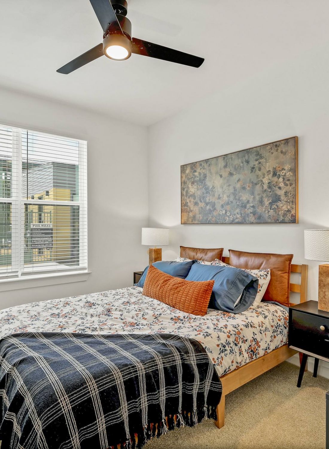 Bright bedroom with a bed, nightstands, lamps, dresser, and large window with natural light. at Bluff View at Frederick Creek.