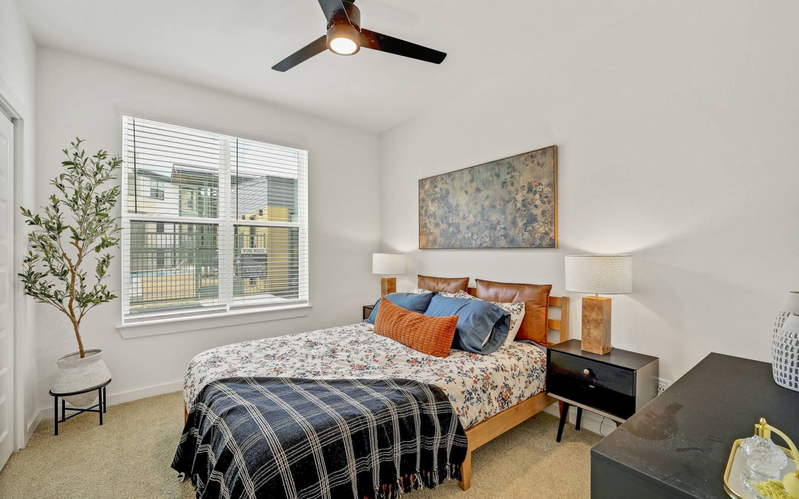 Bright bedroom with a bed, nightstands, lamps, dresser, and large window with natural light. at Bluff View at Frederick Creek.
