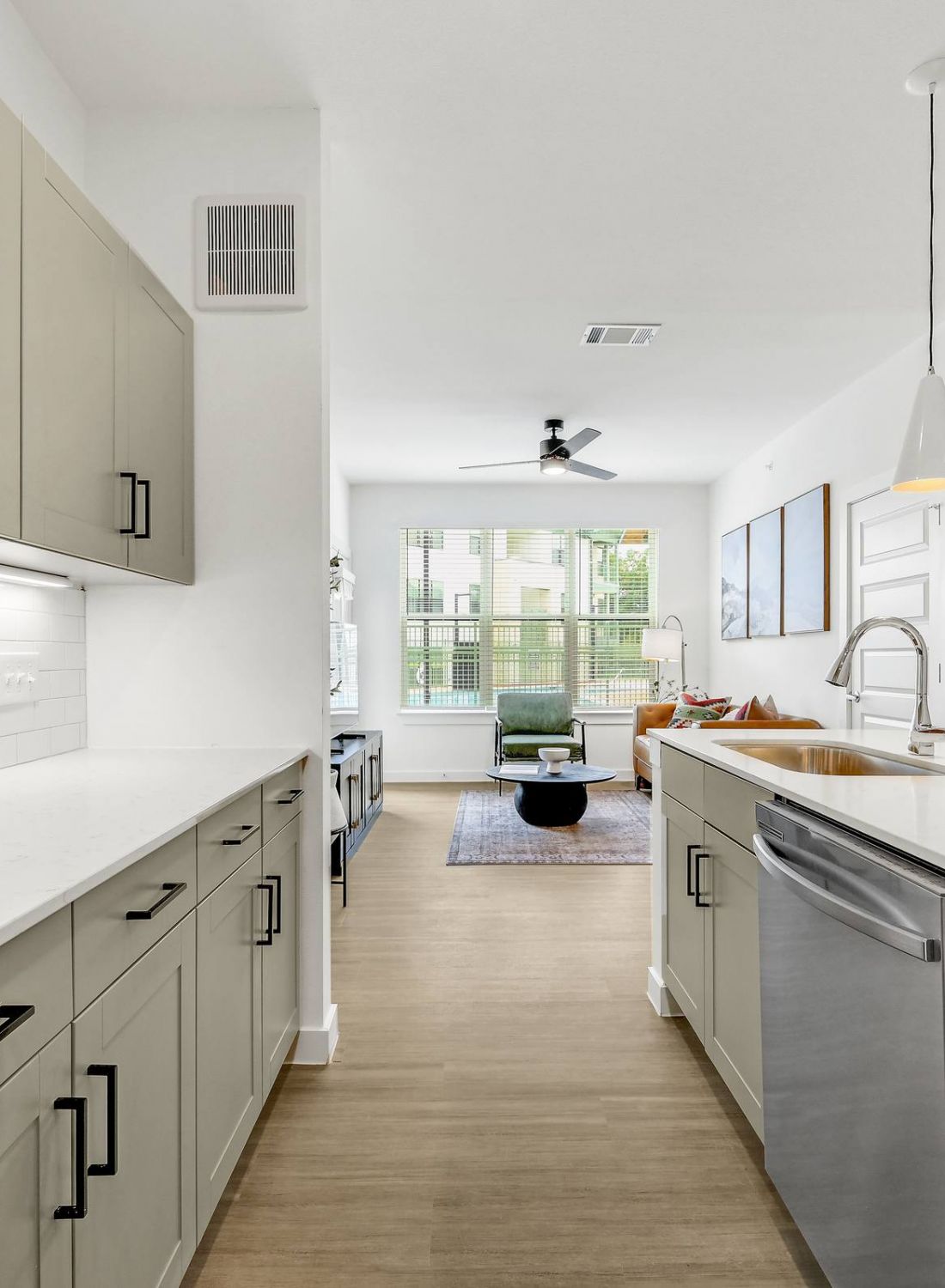Modern kitchen with beige cabinets, white countertops, and stainless steel appliances, leading to a bright living area at Bluff View at Frederick Creek.