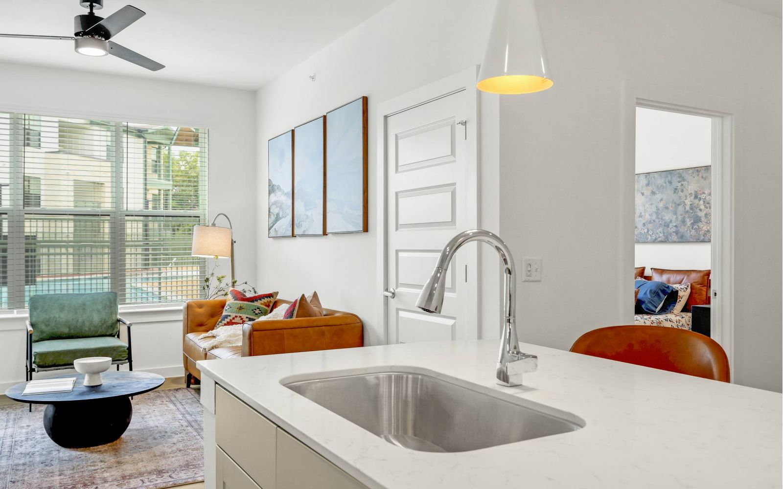 Modern apartment interior with a kitchen island, living area, and a view into a bedroom at Bluff View at Frederick Creek.