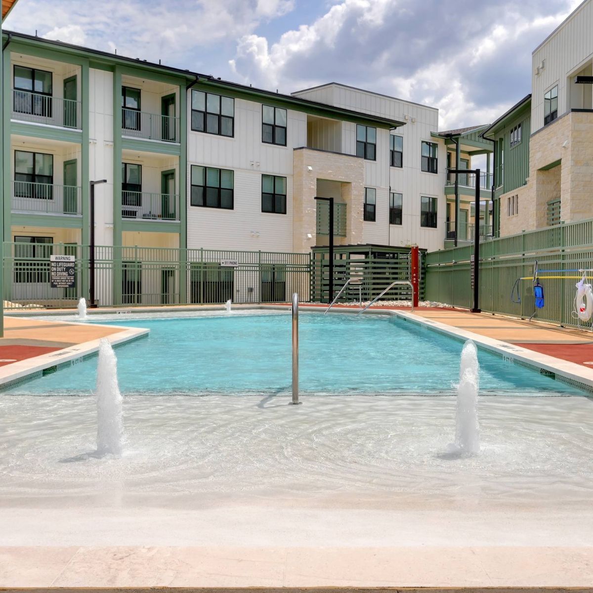 Outdoor apartment pool with fountains in the shallow end, surrounded by modern three-story buildings at Bluff View at Frederick Creek.