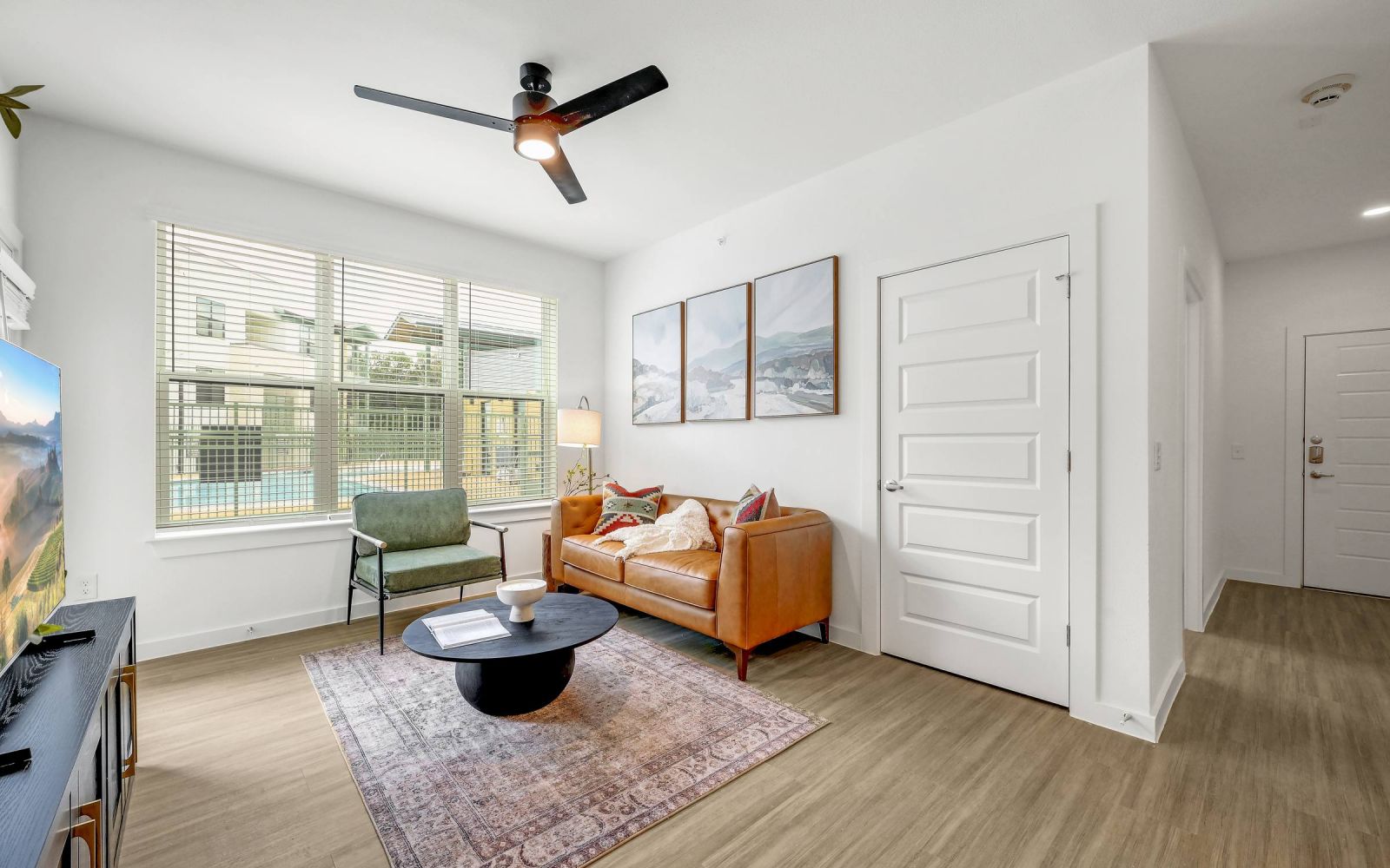 Bright modern living room with tan sofa, round coffee table, green chair, large window, and wall art. at Bluff View at Frederick Creek.