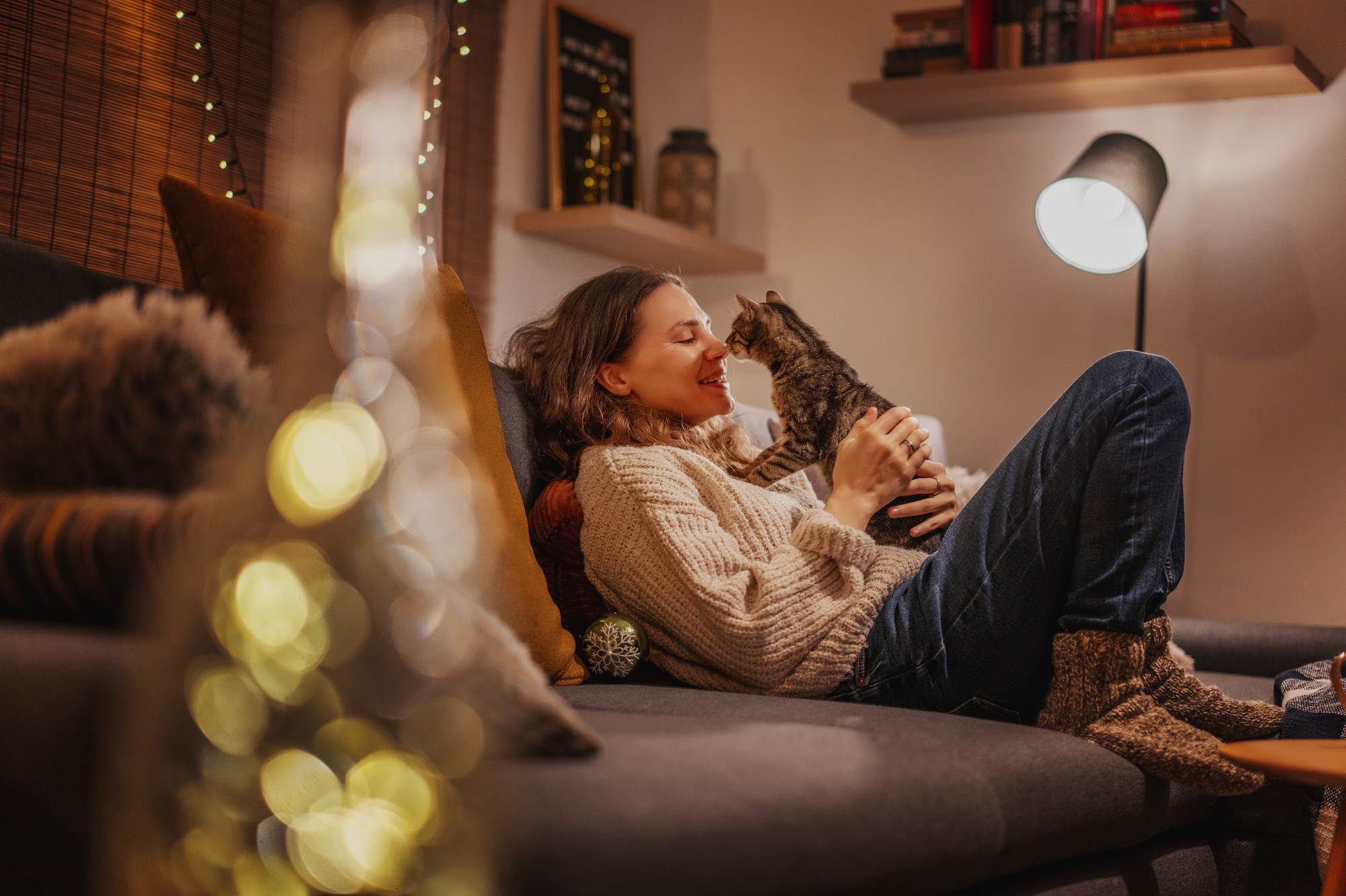 Woman relaxing on a couch, smiling and holding a cat in a cozy, warmly lit living room. at Bluff View at Frederick Creek.