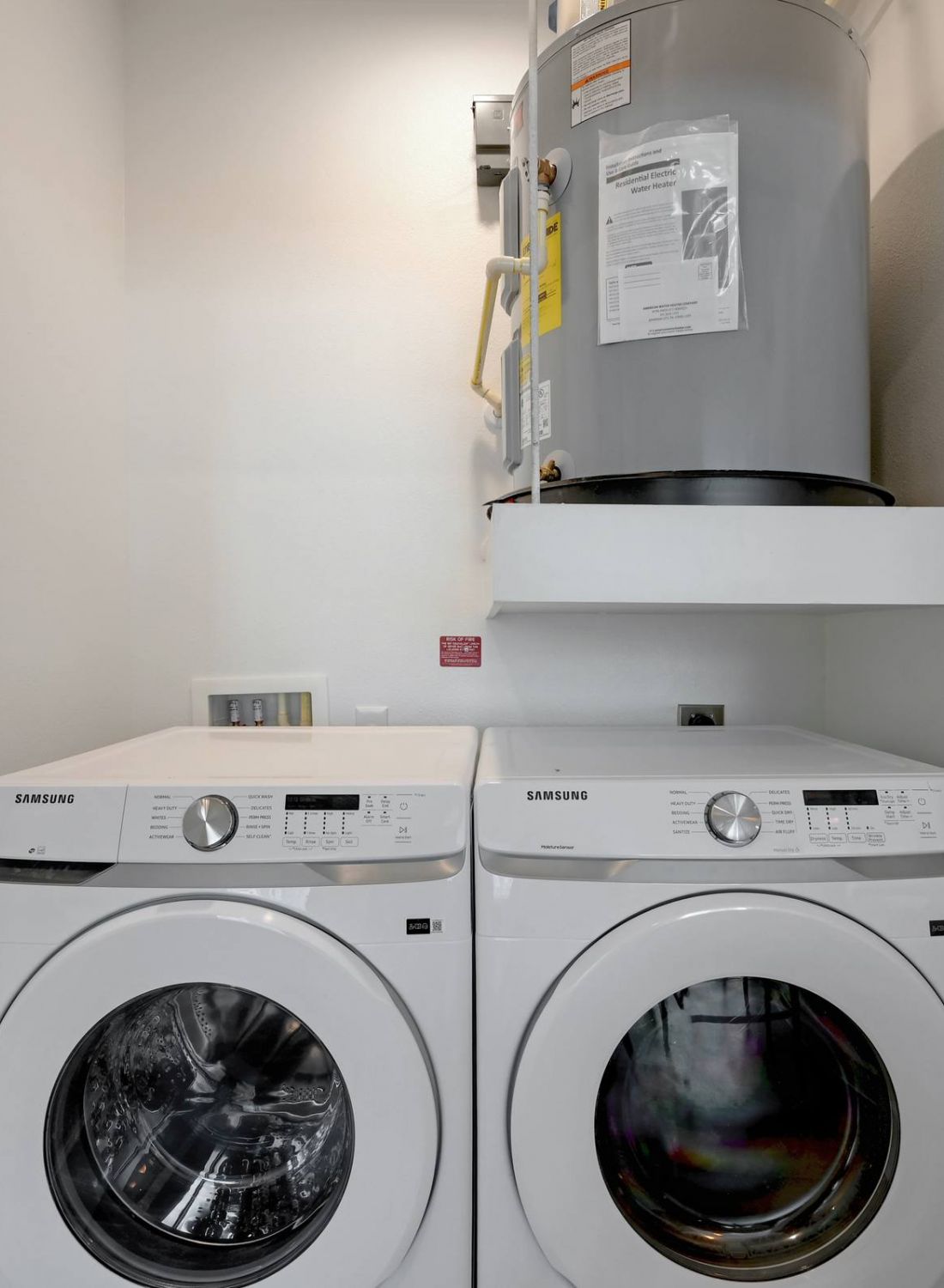 Front-load washer and dryer in a small laundry closet with a water heater on a shelf above at Bluff View at Frederick Creek.