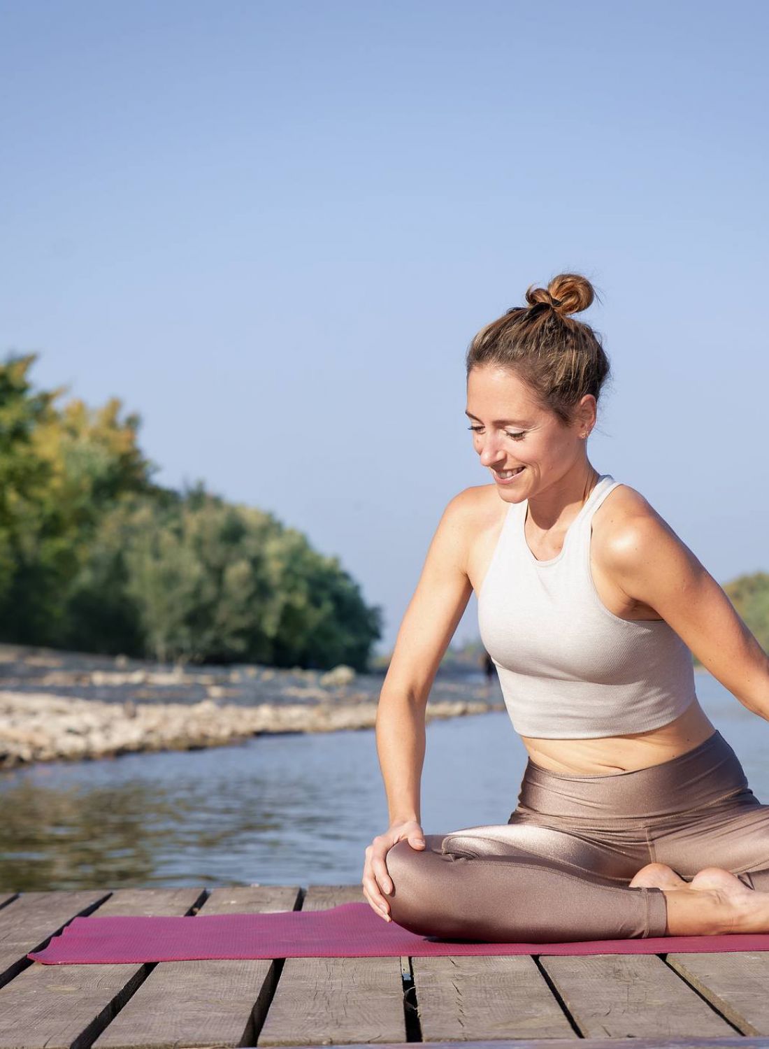 Woman doing yoga in a seated pose on a dock by the water, surrounded by trees, on a sunny day. at Bluff View at Frederick Creek.