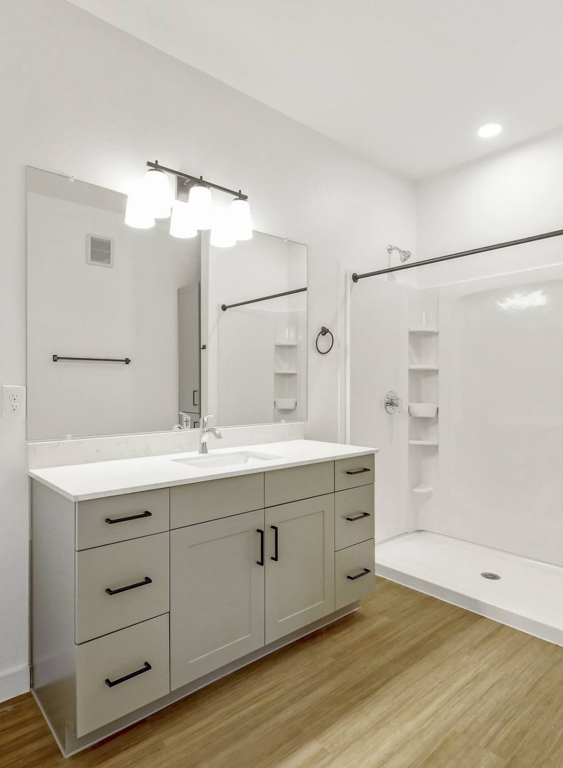Modern bathroom with white walls, large vanity, toilet, and walk-in shower with built-in shelves at Bluff View at Frederick Creek.