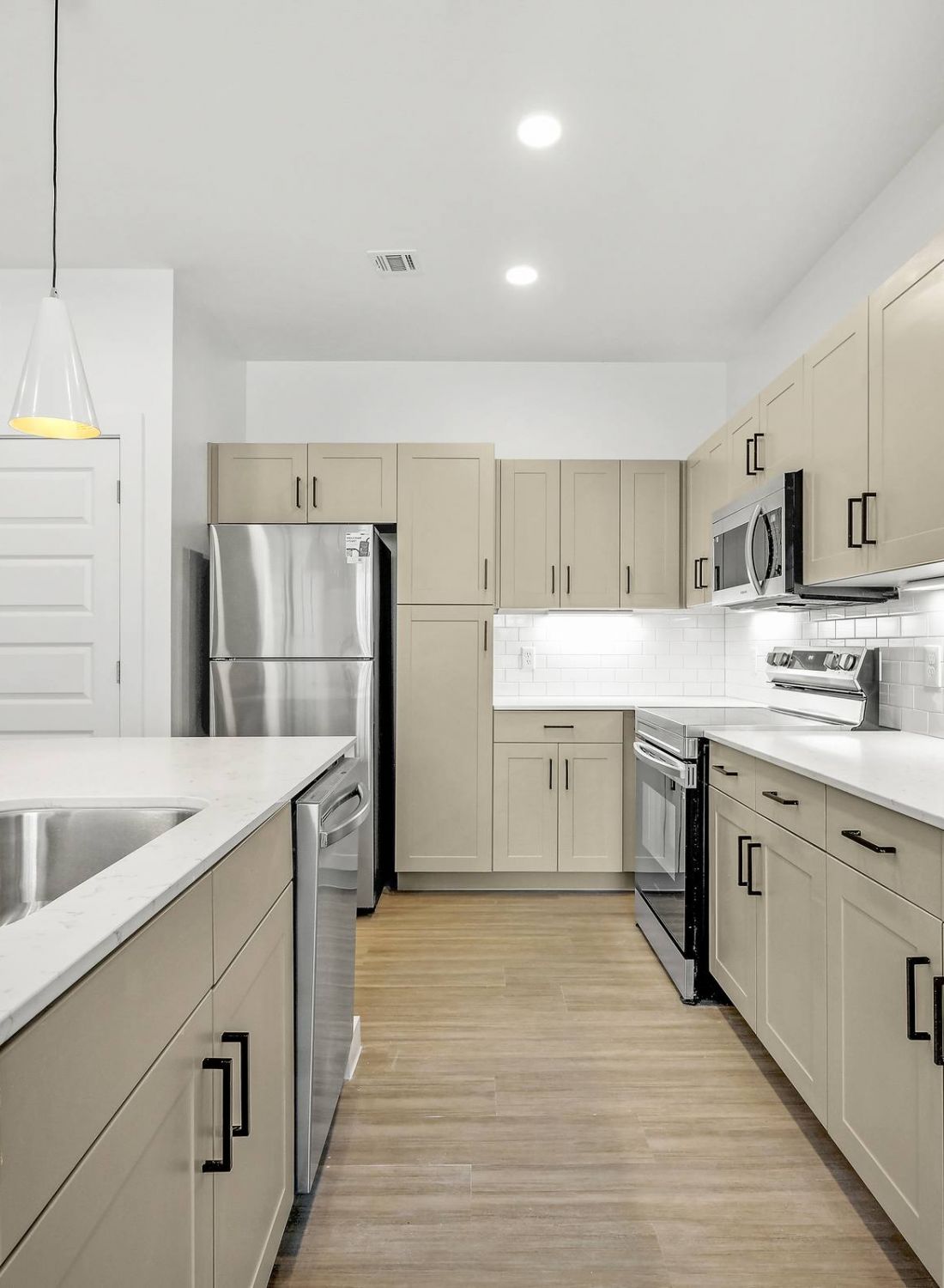 Modern kitchen with beige cabinets, stainless steel appliances, island sink, and white countertops at Bluff View at Frederick Creek.
