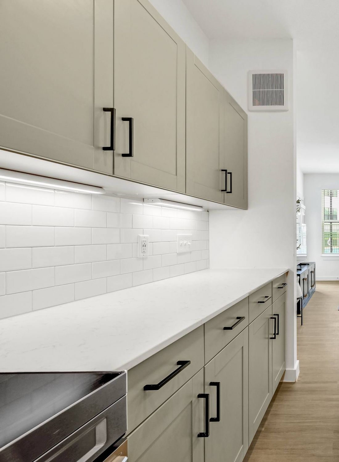 Modern kitchen with beige cabinets, white countertops, and stainless steel appliances, leading to a bright living area. at Bluff View at Frederick Creek.