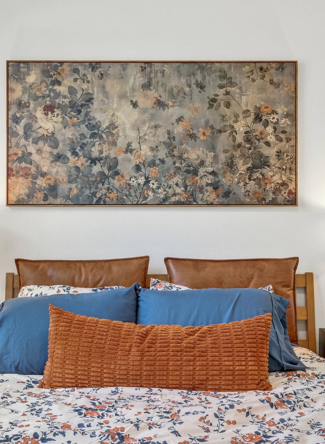 Cozy bed with blue and orange pillows, floral bedding, two lamps, and floral artwork above the headboard. at Bluff View at Frederick Creek.